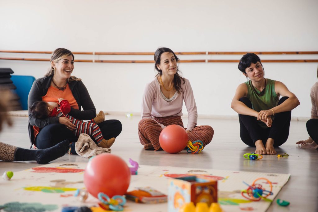 קבוצת אמהות יושבות במעגל עם תינוקות ומשחקים במהלך מפגש תנועה