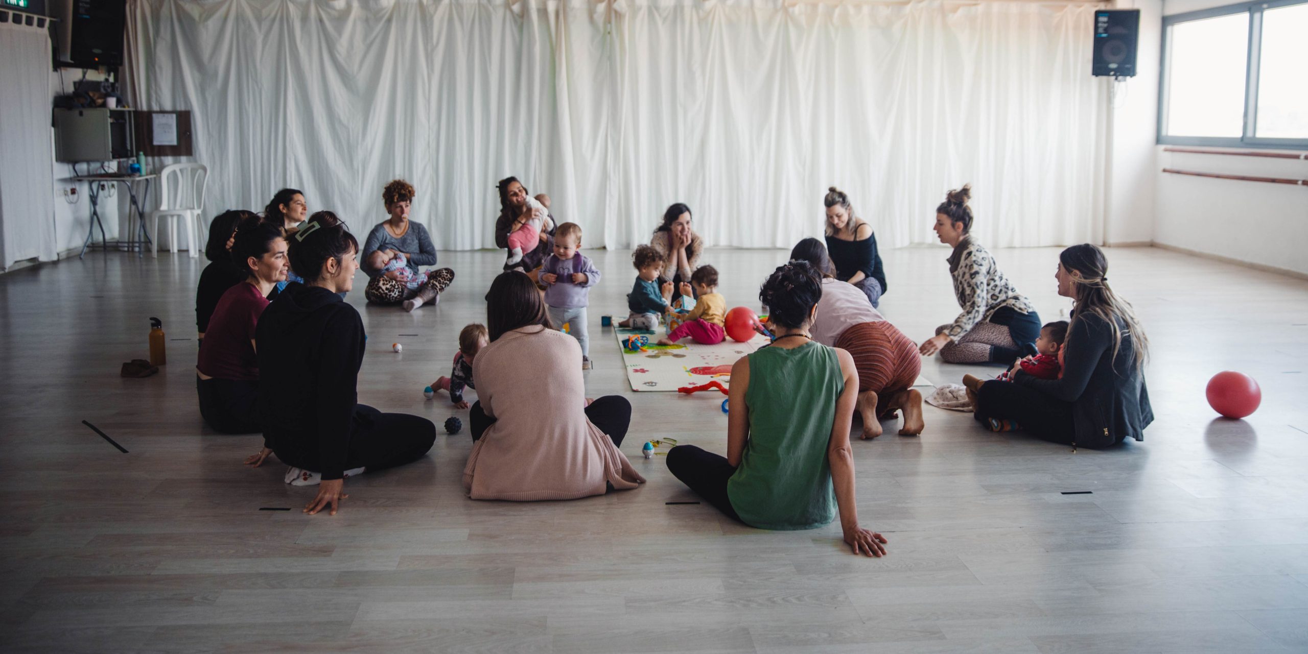 קבוצת אמהות ותינוקות במפגש תנועה במעגל בסטודיו